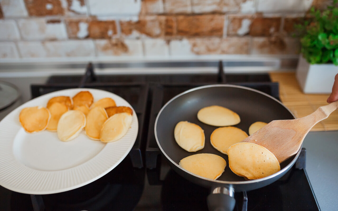 a non-stick skillet on a stovetop with several mini pancakes cooking